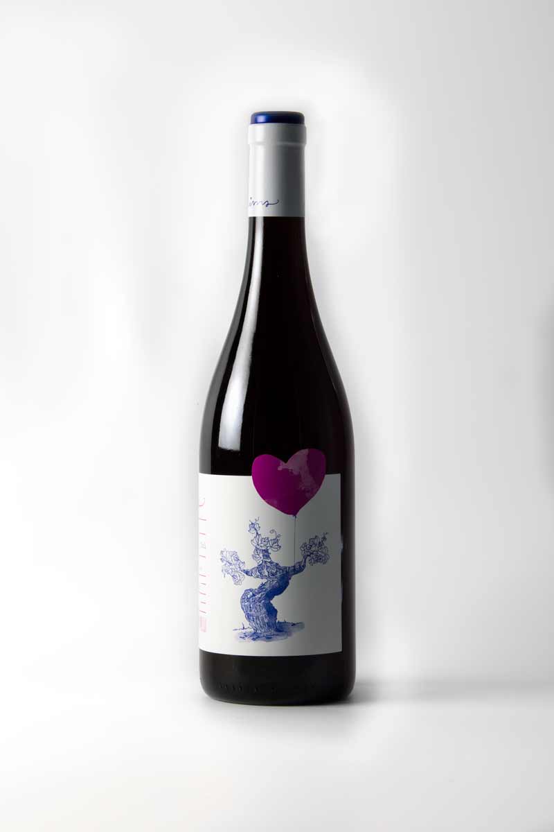 Fotografia de la botella de vi blanc, etiqueta blanca amb un dibuix amb línia blava i un cor amb taca lila.