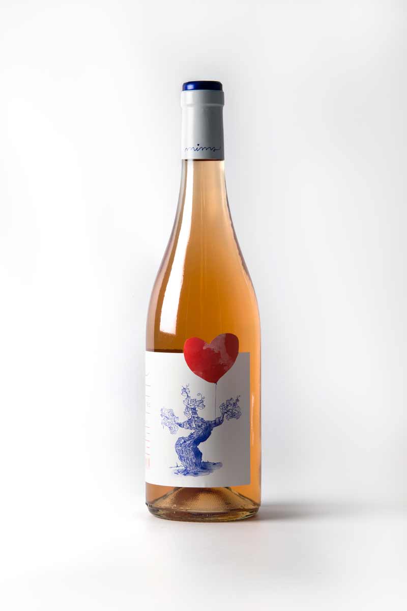 Fotografia de la botella de vi blanc, etiqueta blanca amb un dibuix amb línia blava i un cor amb taca vermell.